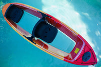 Thumbnail for A top-down view of a red and orange kayak floating on clear turquoise water, featuring two black seats and a transparent hull.